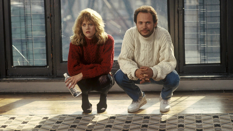 Meg Ryan wearing a red knit sweater crouching next to Billy Crystal wearing a white knit sweater in "When Harry Met Sally..."