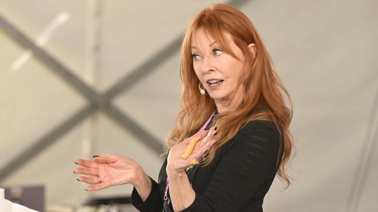 Cassandra Peterson giving a talk wearing a black top with her long, wavy red hair down.