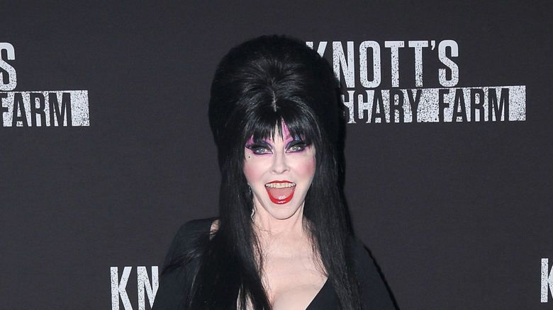 Elvira at a Halloween event wearing her signature black dress with teased black hair and heavy makeup.
