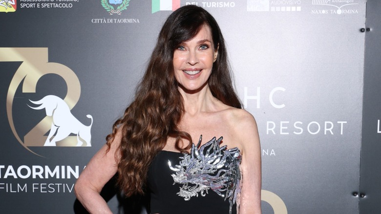 Carol Alt poses in a black strapless gown with silver embellishments along with her long brown hair down in loose curls while attending the 72nd Taormina Film Festival in Italy in 2026.