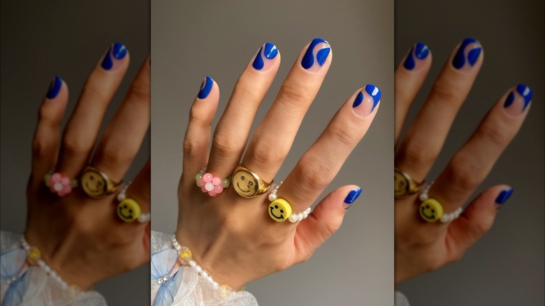 Close up shot of a wavy blue manicure on a hand with several '60s style rings.