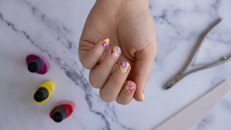 Close up shot of manicured nails with yellow and pink swirl designs.