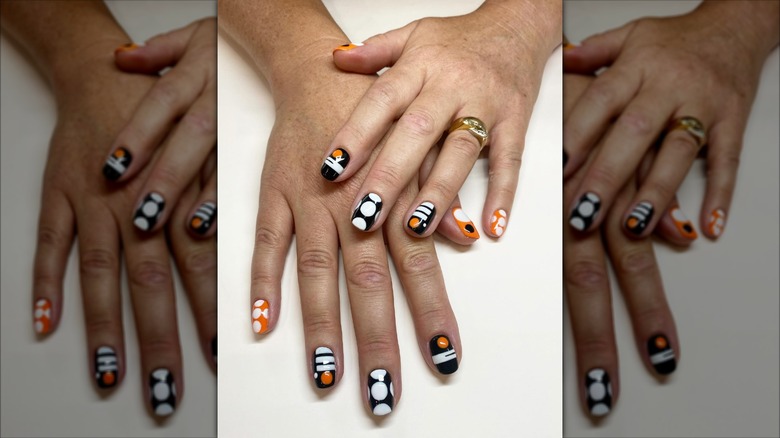 Close up look at a Mod-style manicure with black, white, and orange geometric shapes.