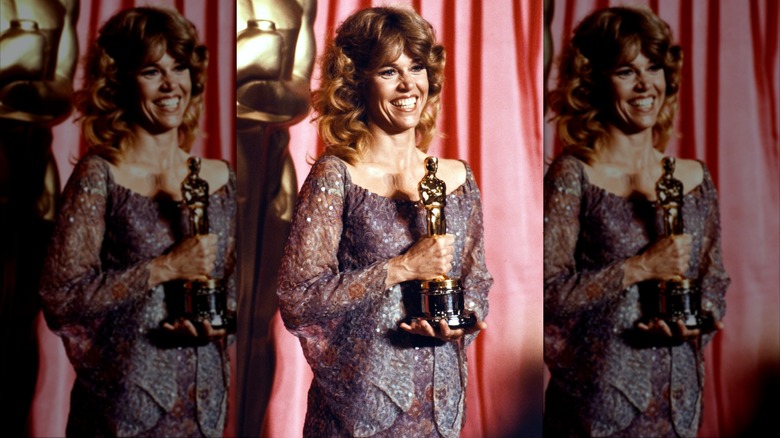 Jane Fonda posing with her Academy Award wearing a flowing purple gown with her hair in curls.