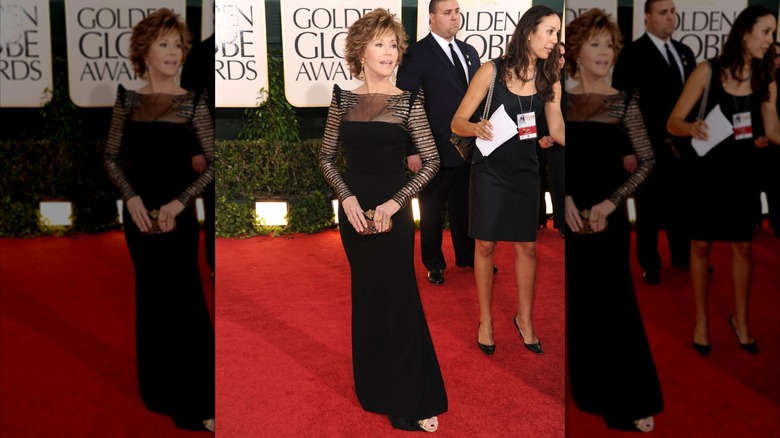 Jane Fonda posing on the Golden Globes red carpet wearing a long black gown with detailed sleeves and shoulders.
