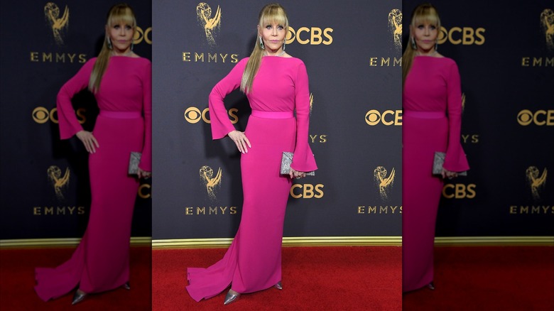 Jane Fonda posing on the red carpet wearing a bright pink gown with her hair in a low ponytail with blunt bangs.