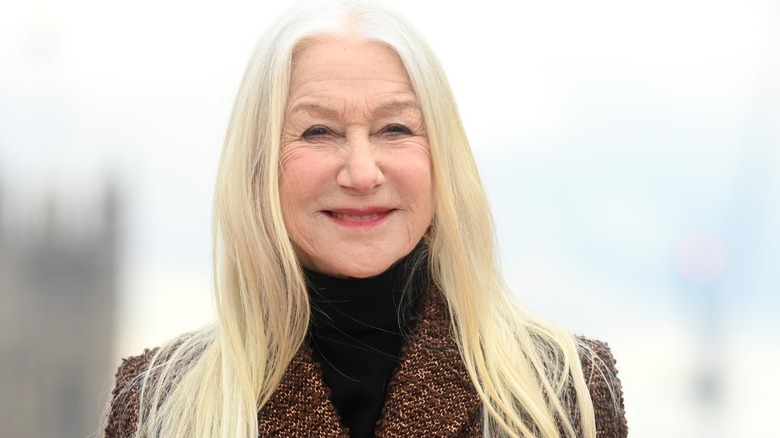 Helen Mirren wore her silver hair down straight with a middle part and a red lip along with a black turtleneck under a brown tweed coat while attending an event for "Shazam! Fury of the Gods" in London, England in 2023.
