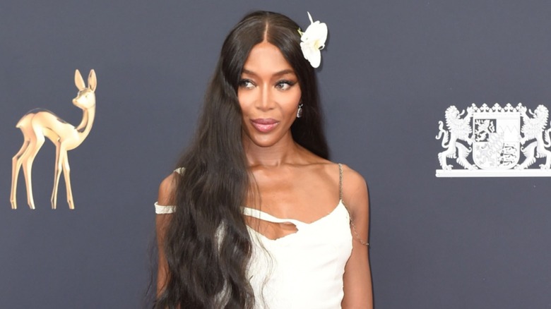 Naomi Campbell wore her black hair down in loose waves and a middle part along with a large white floral hairpiece on one side to match her white dress while attending the 2025 Bambi Awards in Munich, Germany.