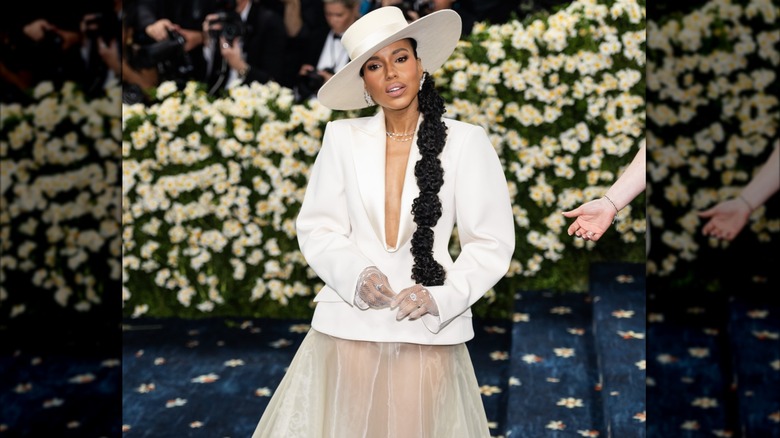 Kerry Washington posing at the 2025 Met Gala wearing a white hat, white top with a plunging neckline, and a sheer tulle skirt.