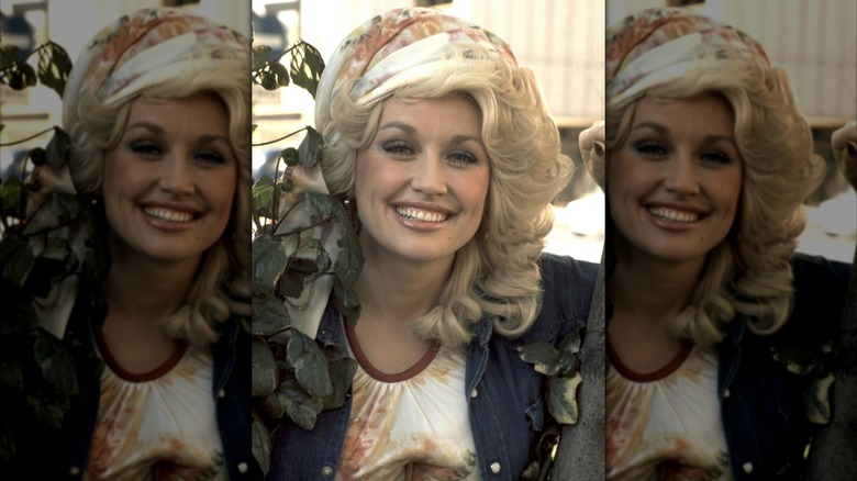 Dolly Parton smiling wearing a head scarf with a denim jacket.