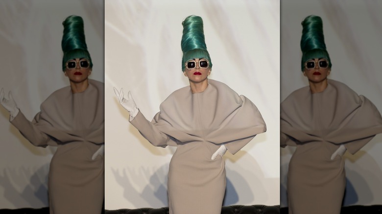 Lady Gaga performing in a beige dress with a teal-green beehive hairdo and sunglasses.