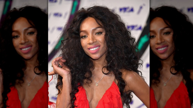 Lil Mama posing at an event wearing a red dress with voluminous curly hair.