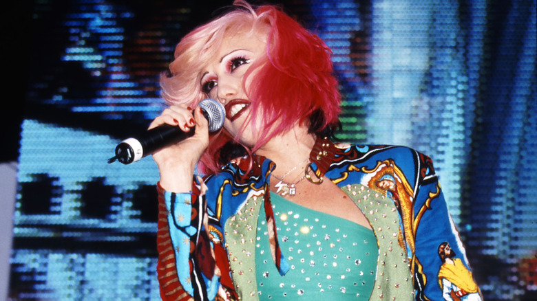 Gwen Stefani of No Doubt performing with pink and blond hair wearing a turquoise shirt and a colorful jacket.