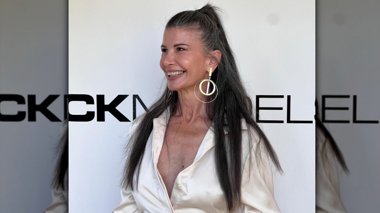 A woman smiling at an event with her hair in a half-up style wearing a silky blouse and statement earrings.