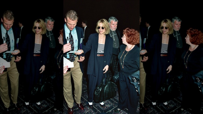 Meg Ryan pictured wearing a navy pantsuit with a striped shirt and sunglasses.