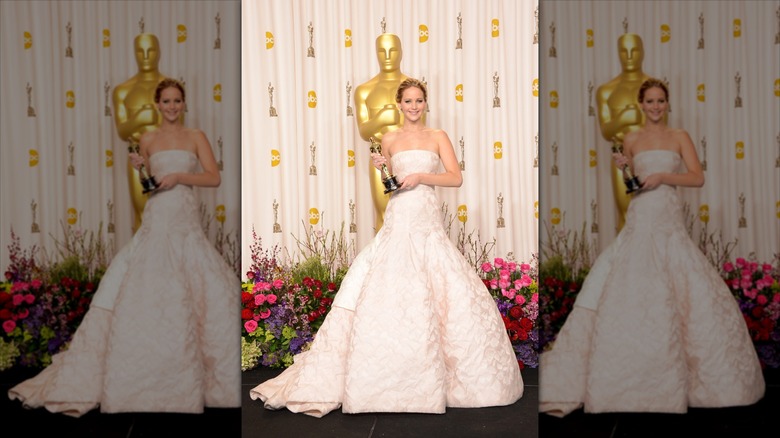 Jennifer Lawrence holds an Oscar Award wearing a white ball gown