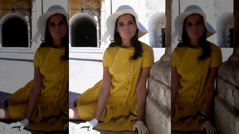Ali MacGraw wearing a yellow wool outfit with white gloves and a white floppy hat.