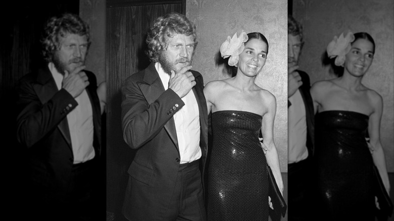 Ali MacGraw wearing a black strapless dress and flower decoration in her hair smiling next to Steve McQueen wearing a suit.