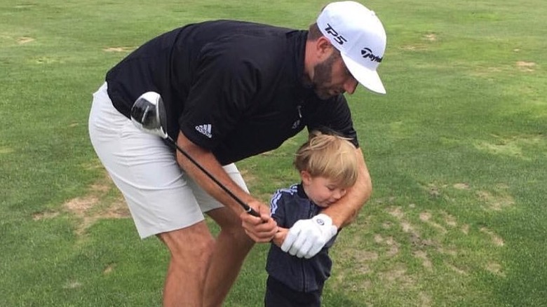 Dustin Johnson helps his son, Tatum Johnson, swing a golf club.