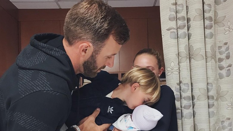 Dustin Johnson holding, Tatum Johnson, as he kisses his newborn brother, River Johnson, who appears to be held by Paulina Gretzky.