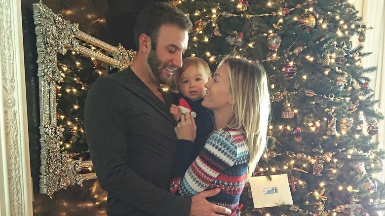 Dustin Johnson and Paulina Gretzky hug their baby, Tatum Johnson, in front of a Christmas tree.
