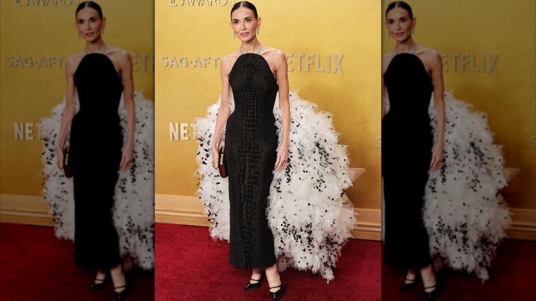 Demi Moore posing on the red carpet in a black halter-top dress with a fluffy white and black train.