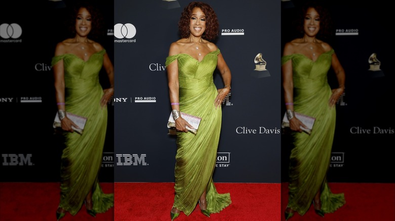 Gayle King posing on the red carpet with her hand on her hip wearing a flowing off-the-shoulder chartreuse gown.
