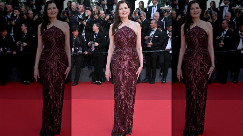 Geena Davis posing on the red carpet wearing a wine-red strapless dress with intricate sequin designs.