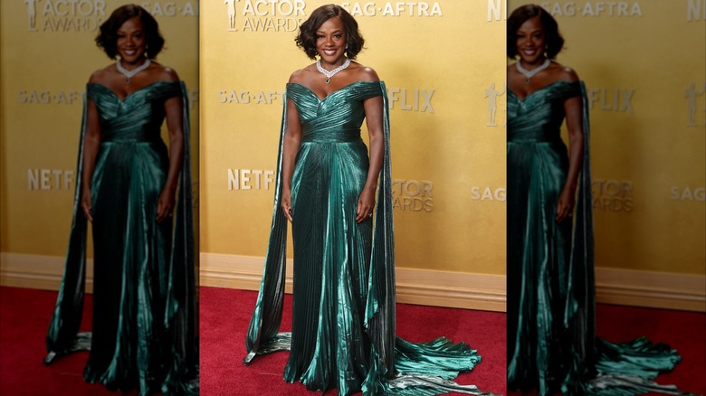 Viola Davis posing on the red carpet in a shiny emerald-green, off-the-shoulder gown with pleated details and a train.