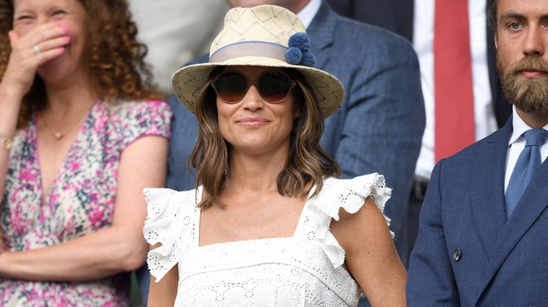 Pippa Middleton wearing a white dress with a beige hat and sunglasses at Wimbledon in 2018.