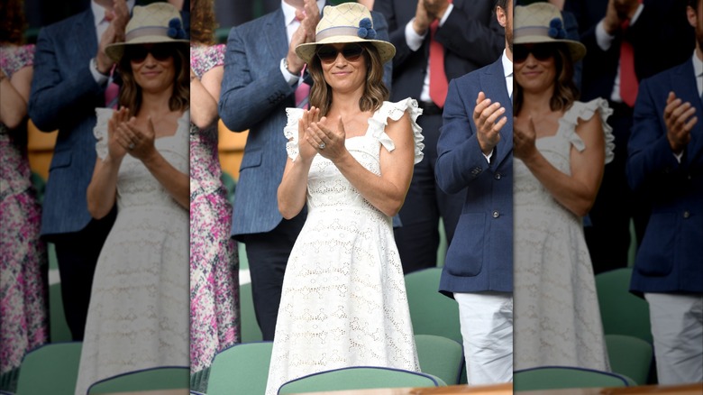 Pippa Middleton clapping wearing a white dress with sunglasses and a fedora at Wimbledon in 2018.