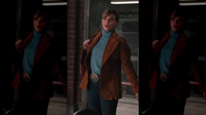 Belle Skinner wearing a turquoise turtleneck and a brown suede blazer