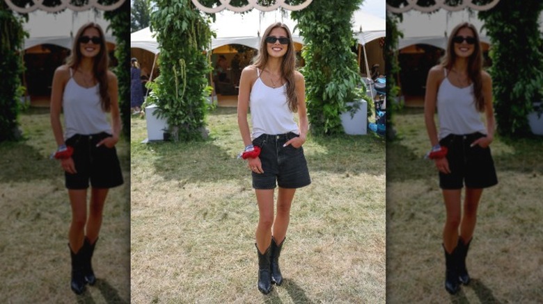 A person posing in a white top with black denim A-line shorts and cowboy boots