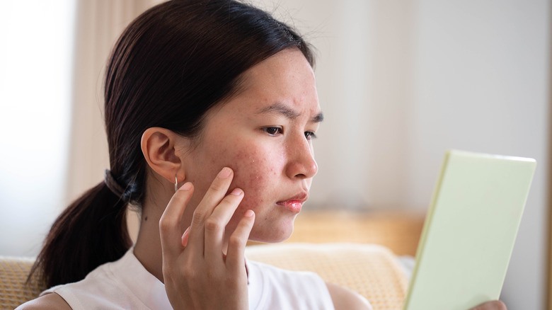 Woman looking at acne in mirror