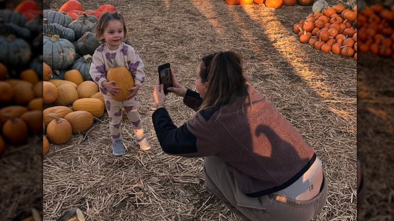 Kaley Cuoco crouches down to take a photo of daughter Matilda at a pumpkin patch.
