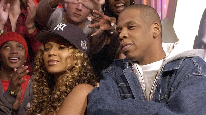 A throwback image of Jay-Z and Beyonce. They are both about 15-20 years younger, and posing shoulder-to-shoulder with their arms crossed.