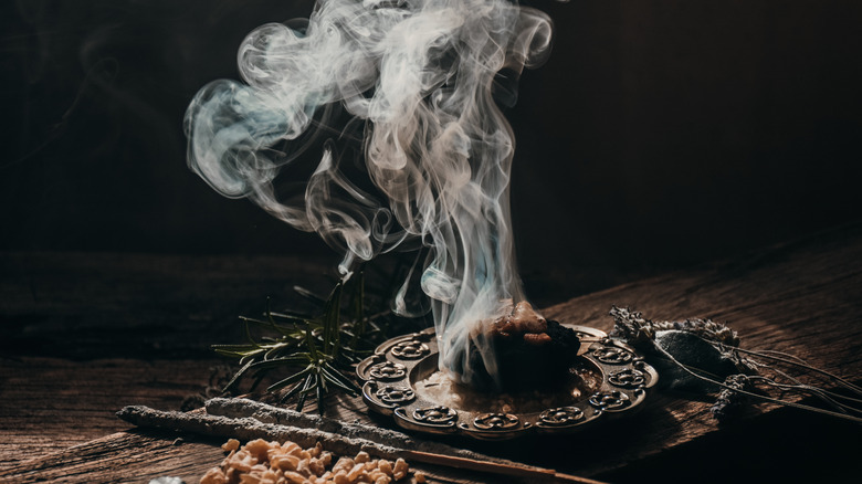 A rustic smoking sage bundle on a dark background