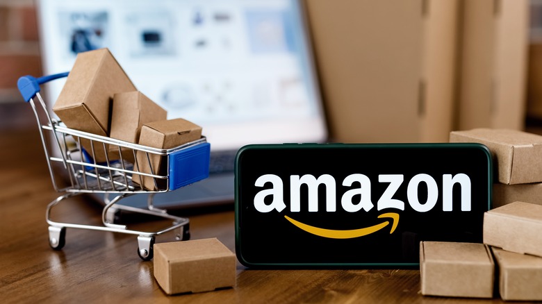 Phone bearing Amazon logo alongside miniature shopping cart full of boxes
