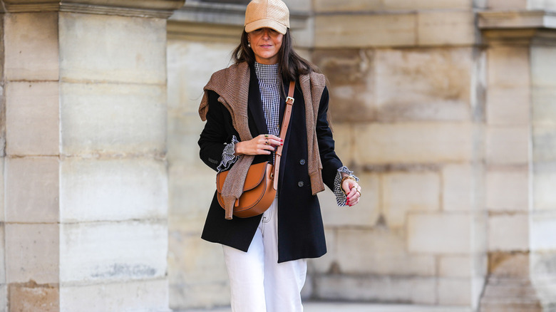 woman wearing beige baseball cap, white pants, blue blazer, and plaid top