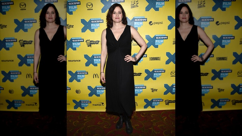 Actress Ally Sheedy posing with her hand on her hip in 2015 wearing a black V-neck dress with black boots.