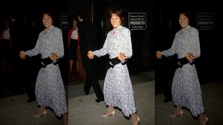 Ally Sheedy wearing a blue floral-print dress with a large black belt.