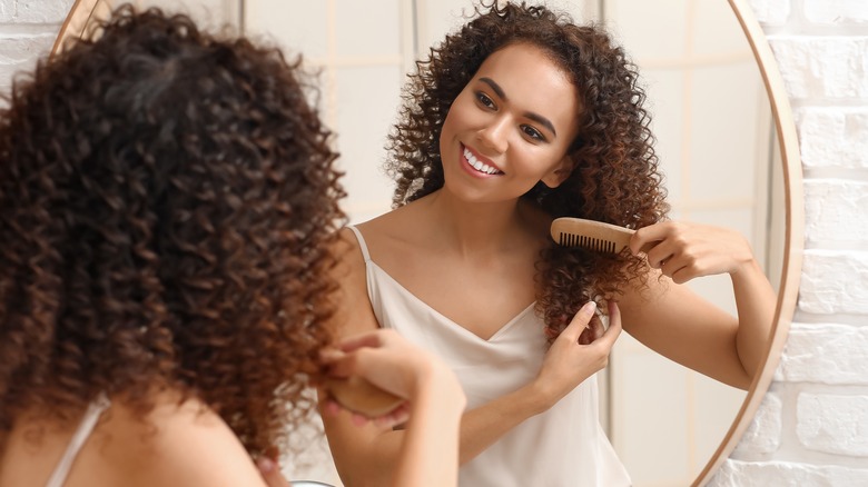 Woman combs naturally curly hair in mirror 