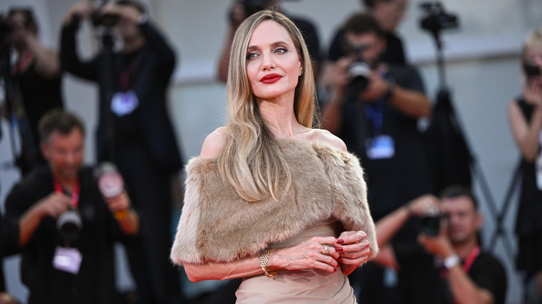 Angelina Jolie smiles wearing red lipstick and a fur stole.