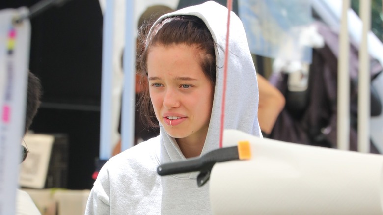 Shiloh Jolie at a farmer's market in Los Angeles wearing a gray hoodie with a lip piercing.