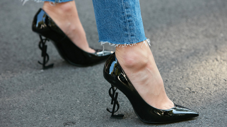 Woman wearing black Saint Laurent logo pumps.