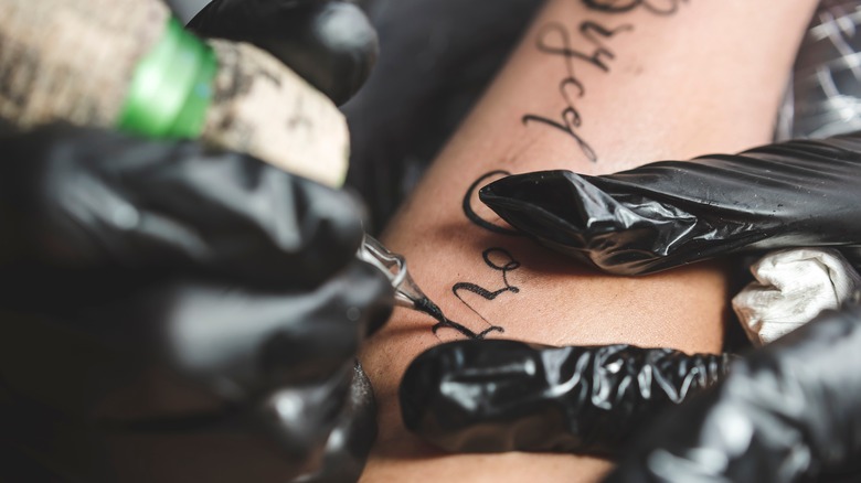 tattoo artist applying black lettering