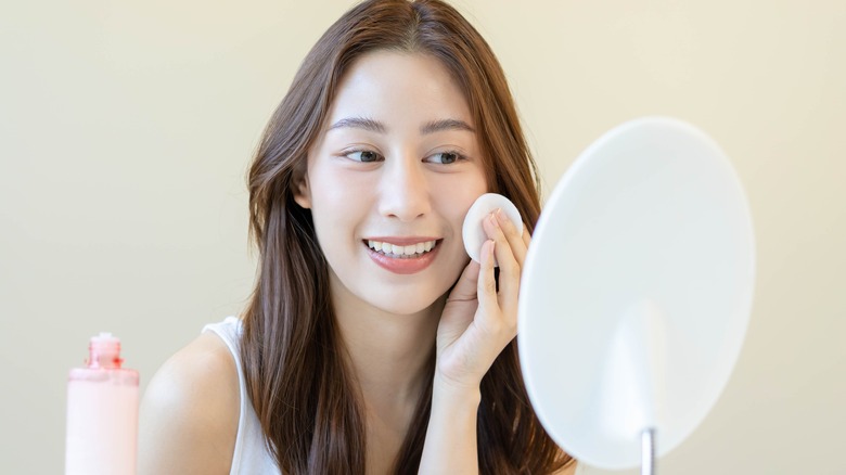 smiling asian girl applying toner on her face