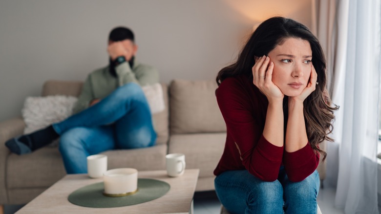 A woman sitting separately from her partner with her head in her hands as he facepalms