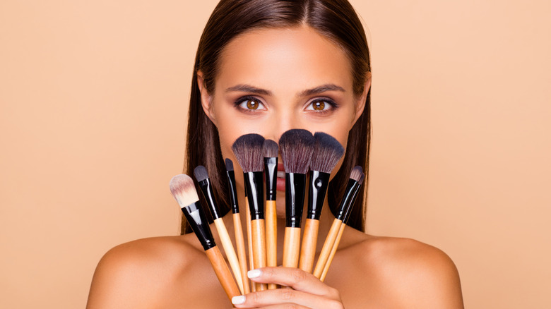 Woman holding many makeup brushes 