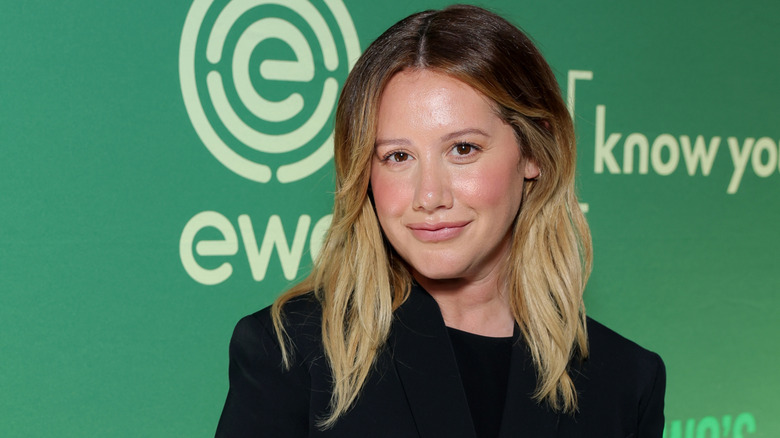 Ashley Tisdale in a black blazer, smiling with her hair down.